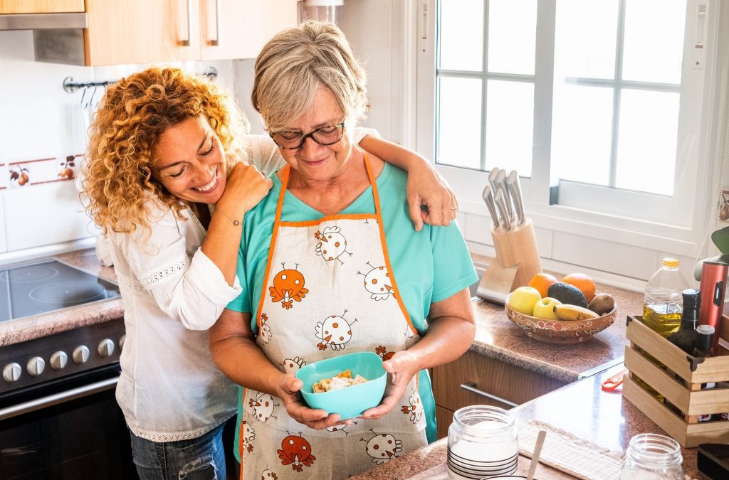 Two women, old and middle age, looking at the homemade baked biscuits smiling in the kitchen